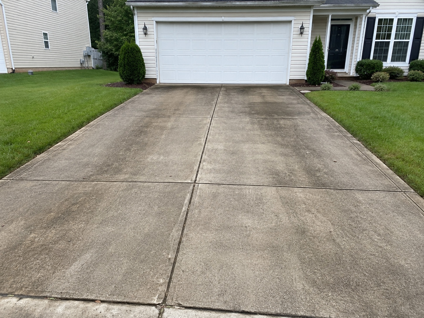 Dirty concrete driveway with dark streaks and organic growth before Fresh Windows pressure washing